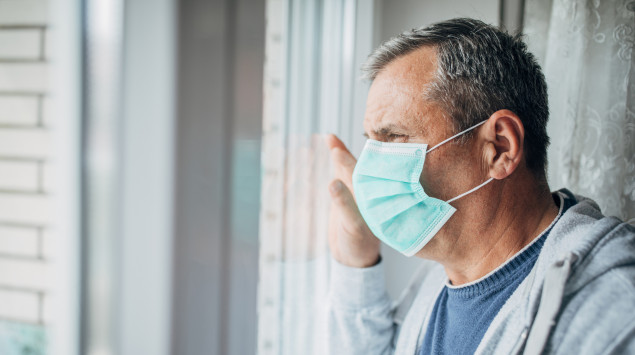 Ein Mann mit Mundschutz schaut aus dem Fenster