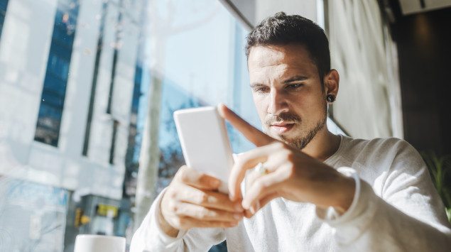 Ein Mann blickt mit ernstem Gesichtsausdruck auf sein Smartphone.