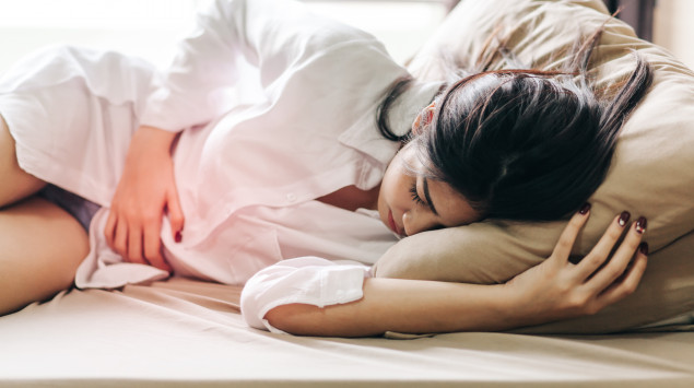 Eine Frau liegt mit Unterleibsschmerzen im Bett