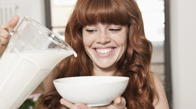 eine junge Frau gießt Milch in eine Schüssel und lacht
