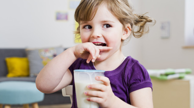 Ein kleines Mädchen hat ein Glas Milch in der Hand