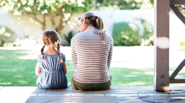 Eine Mutter sitzt mit ihrer Tochter auf einer Treppe: Autismus zeigt sich bereits in der Kindheit
