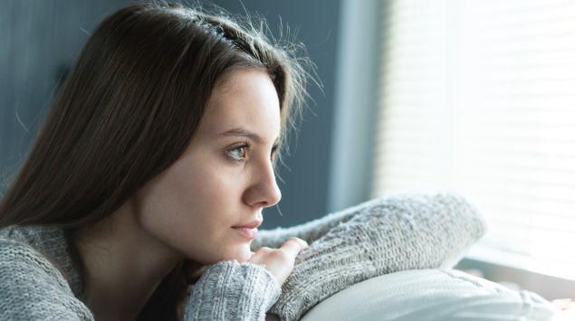 Eine junge Frau blickt nachdenklich aus dem Fenster.