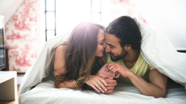 Eine Frau und ein Mann liegen bäuchlings im Bett und schmusen miteinander.
