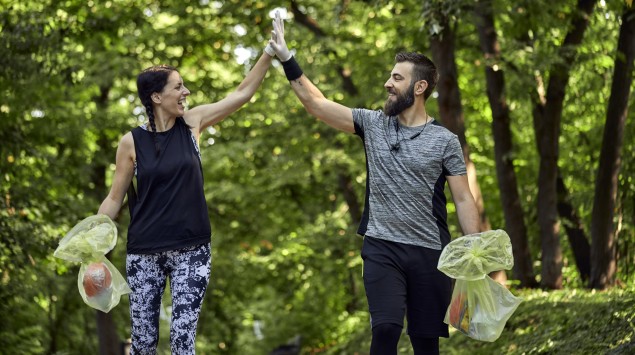 Man sieht einen Mann und eine Frau beim Plogging im Wald.