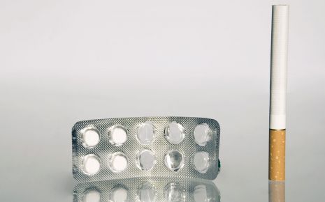 Man sieht eine Zigarette nehmen einem fast leeren Tabletten-Blister.