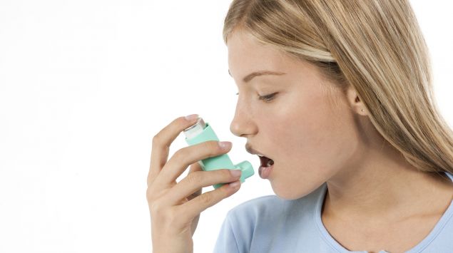 Das Bild zeigt eine Frau, die ein Asthmaspray inhaltiert.