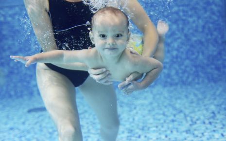 Ein Baby schwimmt unter Wasser und wird von seiner Mutter gehalten.