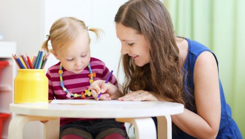 Das Bild zeigt ein kleines Mädchen, das mit seinem Babysitter malt.