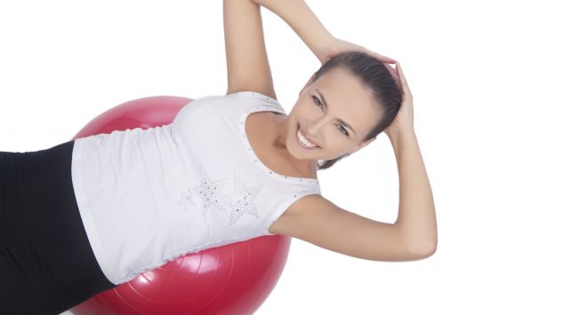 Das Bild zeigt eine Frau in Sportkleidung auf einem Gymnastikball liegend.
