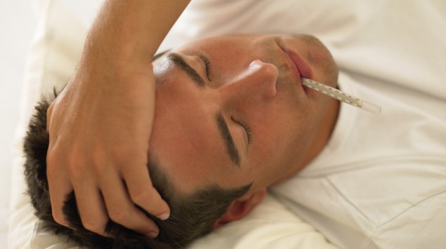 Das Bild zeigt einen Mann mit Kopfschmerzen und einem Fieberthermometer im Mund.