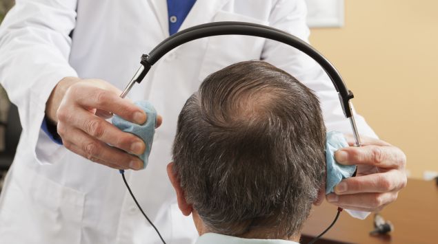 Ein Ohrenarzt setzt einem Mann Kopfhörer für einen Hörtest auf.