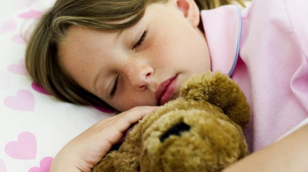 Ein Mädchen schläft im Bett und hält einen Teddy im Arm.
