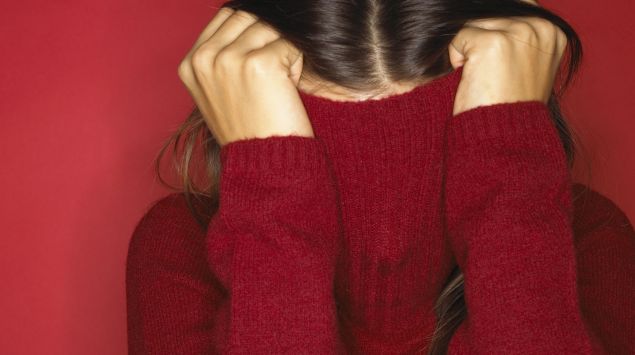 Das Bild zeigt eine Frau, die einen roten Pulli über den Kopf zieht.