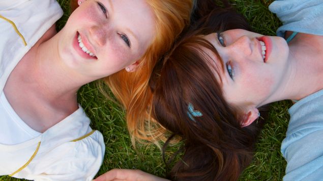 Zwei weibliche Teenager liegen im Gras.