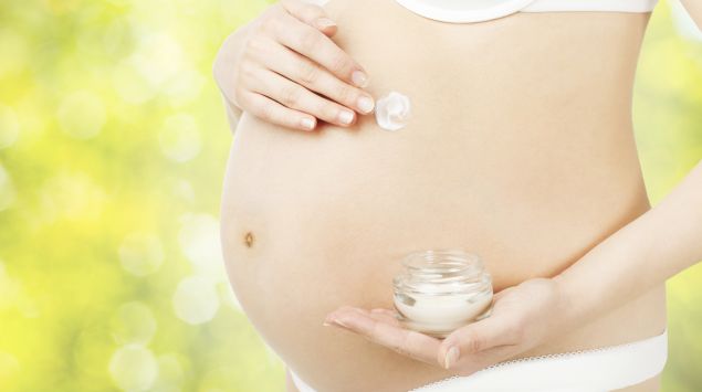 Das Bild zeigt eine schwangere Frau, die ihren Bauch eincremt.
