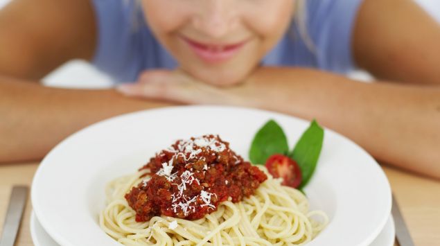 Eine Frau sitzt lächelnd vor einem Teller Spaghetti.