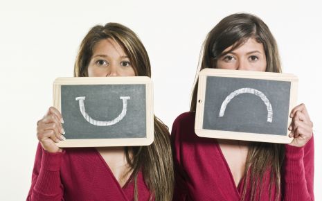 Zwei Frauen, eine mit einem lachenden, eine mit einem traurigen Smiley auf einem Schild.