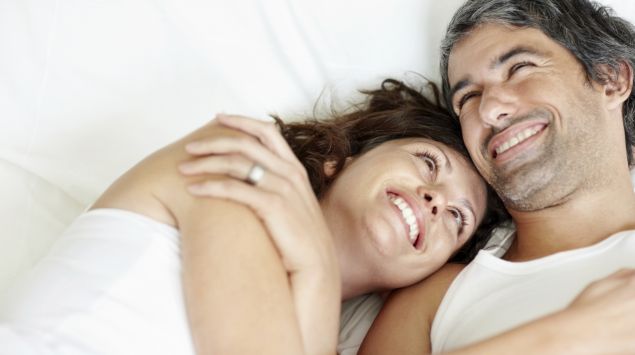Das Bild zeigt ein lächelndes Paar auf einem Bett liegend.