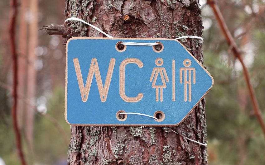 Ein WC-Schild hängt an einem Baum.