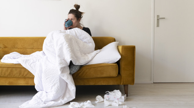 Eine Frau sitzt mit Decke und Tee auf dem Sofa