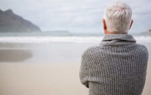 Ein älterer Mann steht am Strand und schaut aufs Meer.