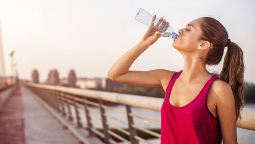 Das Bild zeigt eine sportliche Frau, die aus einer Wasserflasche trinkt.