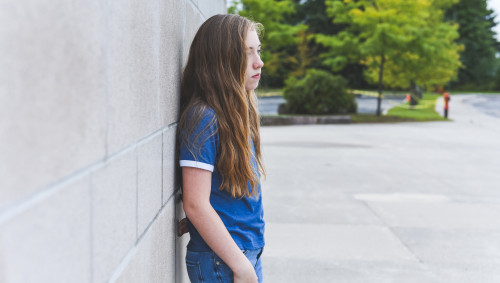 Ein Mädchen in der Pubertät steht einsam auf dem Schulhof.