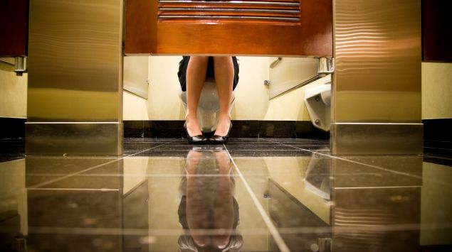 Frau sitzt auf öffentlicher Toilette hinter geschlossener Tür