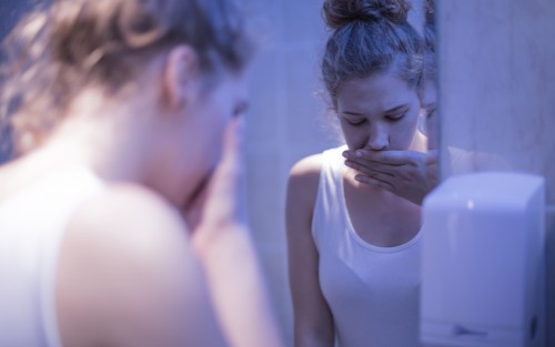 Das Bild zeigt eine junge Frau, die vor einem Spiegel steht und die Hand vor dem Mund hält.